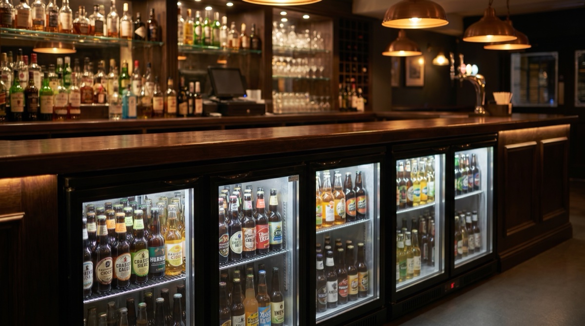 Barra de pub con botellero refrigerado iluminado bajo mostrador de madera oscura en local nocturno